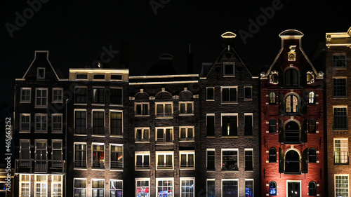 Famous houses in city of Amsterdam at night. Typical Dutch houses with colorful facades. Dancing houses and river canal in Netherland.