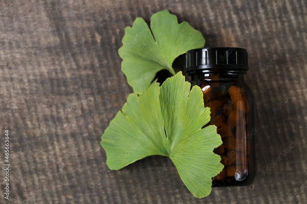 Ginkgo biloba pills .Brown glass jar with homeopathic white pills with ginkgo extract and ginkgo leaves on wooden background . Alternative medicine and homeopathy. Ginkgo biloba pills .Brown glass jar with homeopathic white pills with ginkgo extract and ginkgo leaves on wooden background . Alternative medicine and homeopathy.