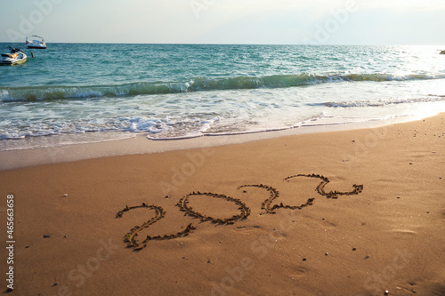 2022 Happy new year concept. Top view of 2022 numbers written on the sand of coastline with wave.Message hand written in golden sand on beautiful sunset or sunrise golden sky background 