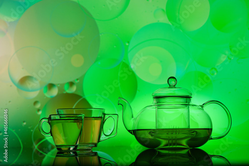 transparent glass teapot and cups with tea and oily drops on colorful background 