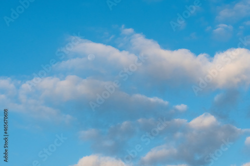 A calming peacful image of puffy white cloused floating in front of the moon in the clear blue sky.