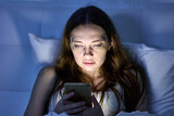 Woman lies in bed and uses phone in evening.