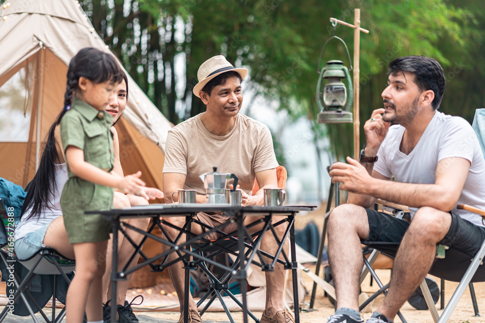 Obraz premium Summer camping in the mountains, spruce forest on background..Back view group of tourists having a rest together around campfire, enjoying fresh air near tent.