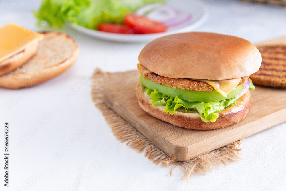 una hamburguesa vegetariana con tomate, lechuga, queso sobre una tabla de madera una hamburguesa vegetariana con tomate, lechuga, queso sobre una tabla de madera