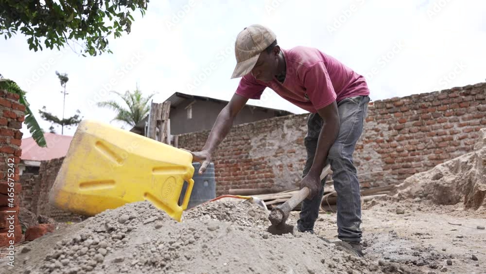 Constructing a traditional house in Africa. African worker Man making cement pouring a jerrycan of water. Rural zone of Uganda. Constructing a traditional house in Africa. African worker Man making cement pouring a jerrycan of water. Rural zone of Uganda.