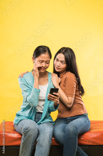 a girl cries sadly looking mobile phone while leaning on her friend's shoulder