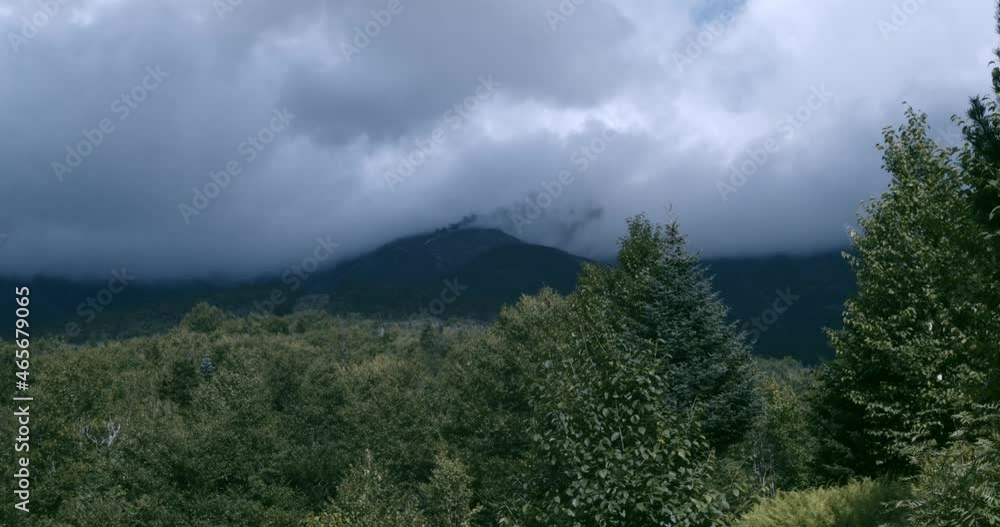 Dark clouds rest on Mount Washington as smoke from the cog railway is visible. The camera tilts revealing trees and tables in the foreground. Dark clouds rest on Mount Washington as smoke from the cog railway is visible. The camera tilts revealing trees and tables in the foreground.