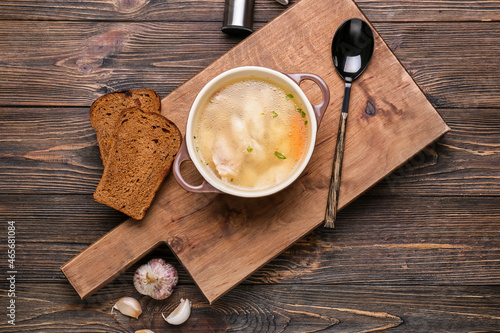 Board with bowl of tasty dumpling soup, bread and garlic on wooden background