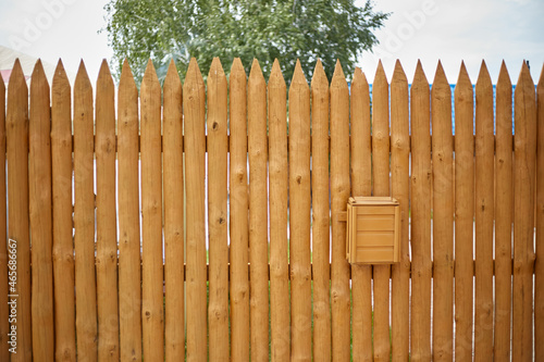 The fence is made of wooden planks in the form of a palisade, a mailbox hangs on it