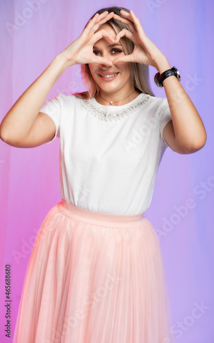 beautiful woman portrait in studio. heart. A girl in a white blouse, a T-shirt and a pink, peach pleated skirt laughs, spins, dances. colored, crimson purple background. holiday, new year, birthday
