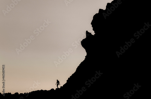 Silhouette of man climbing rock on beach during sunset