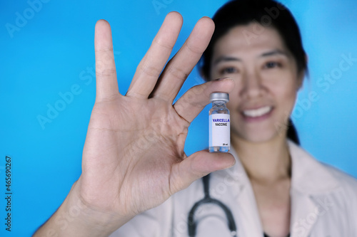 An attractive female doctor in white coat and stethoscope around her neck is holding a glass bottle of chickenpox vaccine, also known as varicella-zoster virus. Healthcare And Medical concept. photo