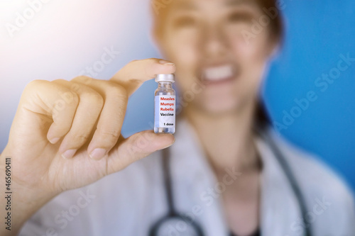 MMR vaccine or measles, mumps, and rubella. Female doctor wearing a white coat with a stethoscope around her shoulder holding a glass vial of M-M-R vaccine, smiling. Healthcare And Medical concept. photo