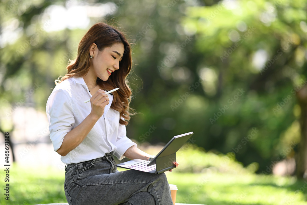 Pretty young woman sitting on bench in park and using digital tablet. Pretty young woman sitting on bench in park and using digital tablet.