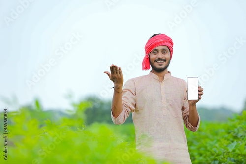 Young indian farmer showing smartphone screen at agriculture field.