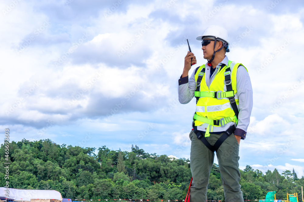 engineer wearing safety harness use using walkie-talkie while working on roof top engineer wearing safety harness use using walkie-talkie while working on roof top
