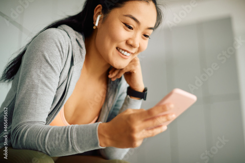Happy Asian athletic woman uses smart phone during break at gym's locker room.