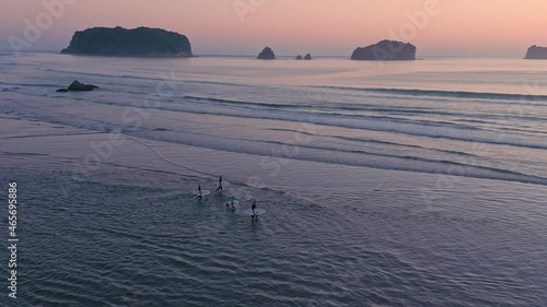 Aerial: A group of Surfers entering water at sunrise. In the background are islands.  Whangamata, Coromandel Peninsula, New Zealand. 6 February 2018.