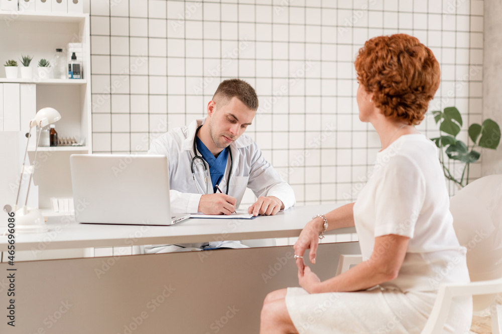 Obraz premium General Practitioner. Male physician and female patient. Patient Having Consultation With male Doctor In Office