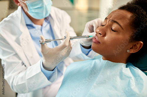 African American woman receives anesthetic during dental procedure at dentist s office.
