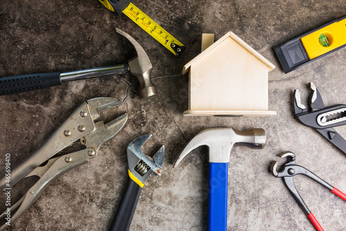 Wooden white house toy and construction tools on Gray-black cement floor background with copy space.Real estate concept, New house.Home repair concept