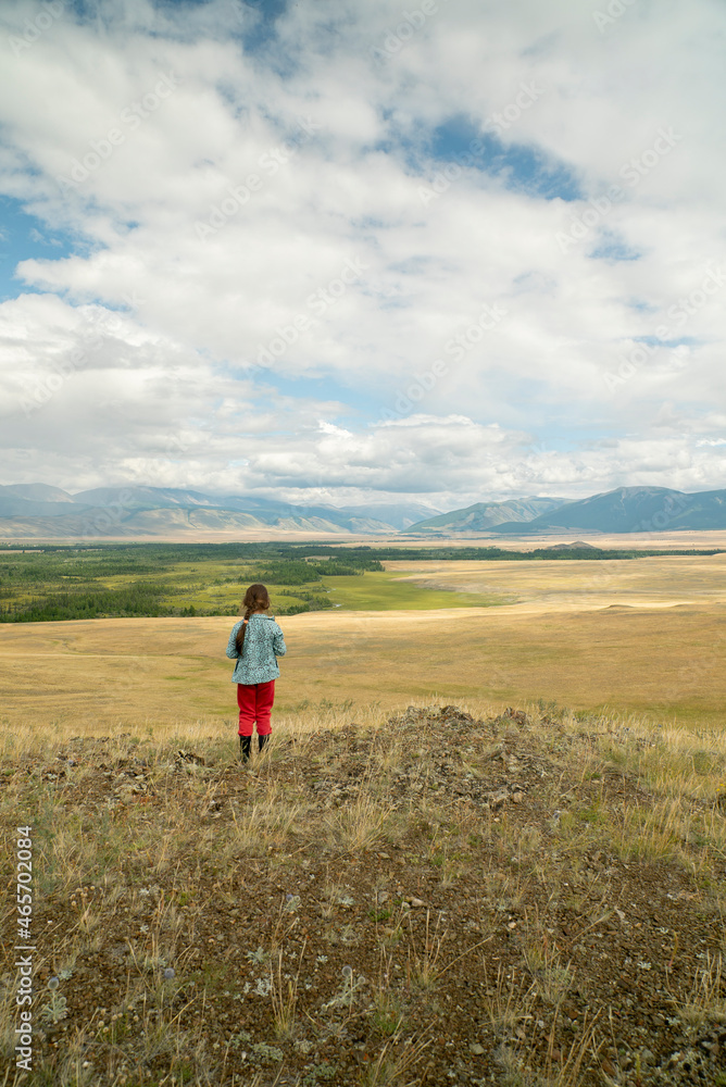 The girl in a picturesque place looks at the mountains and the steppe