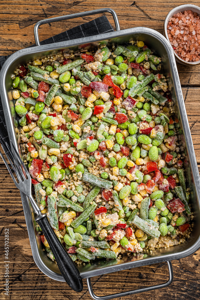Mix of frozen raw vegetables and quinoa in a kitchen tray. Wooden background. Top view