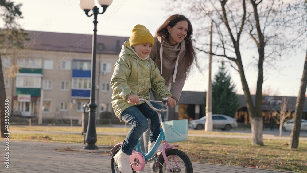 mother teaches little child to ride bike in the city, kid rides on sidewalk, happy family, baby plays and laughs with mom, learn ride, make childhood dream come true girls, daughter and mom are funny