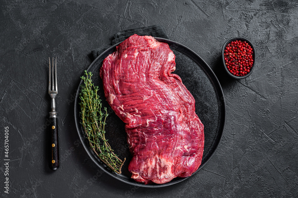 Flank or flap raw beef steak on plate with thyme. Black background. Top view