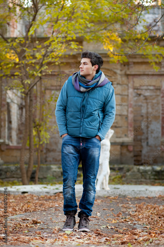 Young man hiking in autumn park, outdoor portrait, with abandoned old style building
