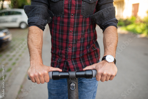 Close up of a man driving an electrical scooter on the street wearing a watch