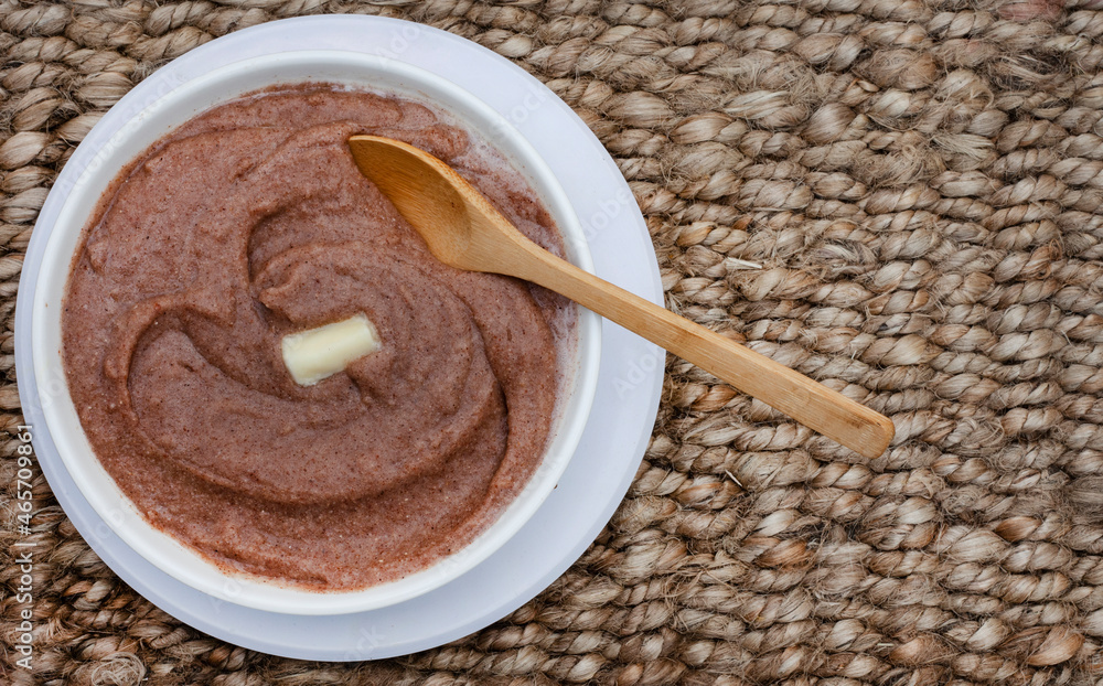 Traditional African sorghum porridge on rustic woven surface in a white bowl with butter and wooden spoon with copy space Traditional African sorghum porridge on rustic woven surface in a white bowl with butter and wooden spoon with copy space