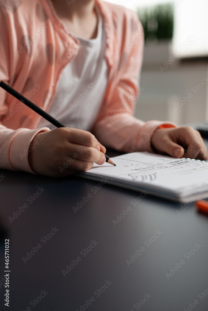 Closeup of little schoolchild writing mathematics homework on notebook during classroom lesson sitting at desk table in living room. Concept of home schooling, distance learning, online education Closeup of little schoolchild writing mathematics homework on notebook during classroom lesson sitting at desk table in living room. Concept of home schooling, distance learning, online education