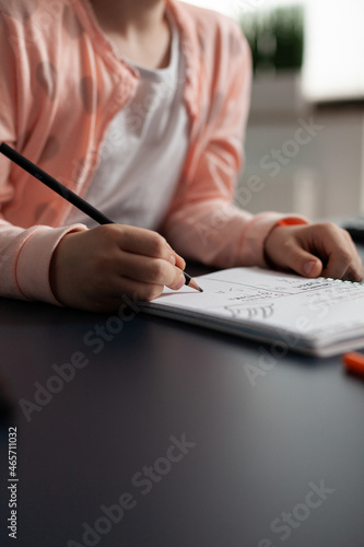 Closeup of little schoolchild writing mathematics homework on notebook during classroom lesson sitting at desk table in living room. Concept of home schooling, distance learning, online education