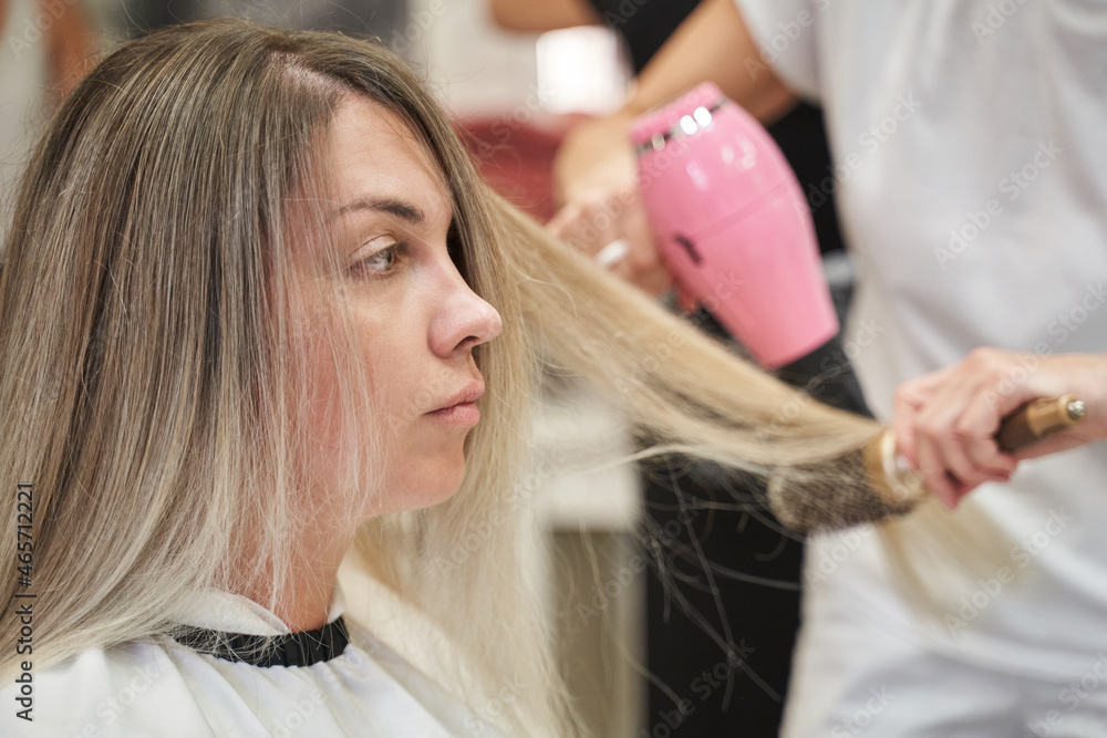 Fototapeta premium hairdresser blow-dry the hair of a young woman with long white hair pulling it on with a round comb