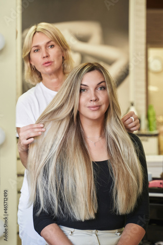 the hairdresser straightens in front of the mirror very long beautiful blond hair of a woman who smiles