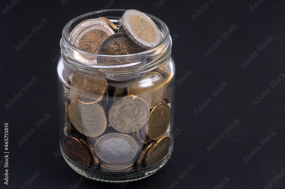 Bocal transparent de pièces de monnaie sur fond noir Bocal transparent de pièces de monnaie sur fond noir