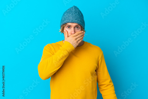 Handsome blonde man isolated on blue background covering mouth with hand