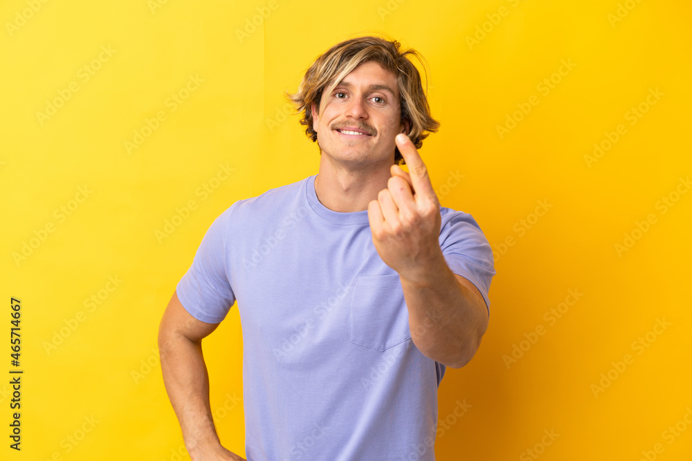 Handsome blonde man isolated on yellow background doing coming gesture Handsome blonde man isolated on yellow background doing coming gesture