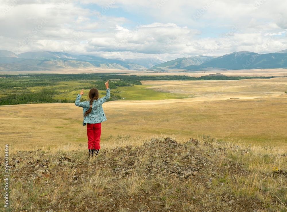 The girl in a picturesque place looks at the mountains and the steppe