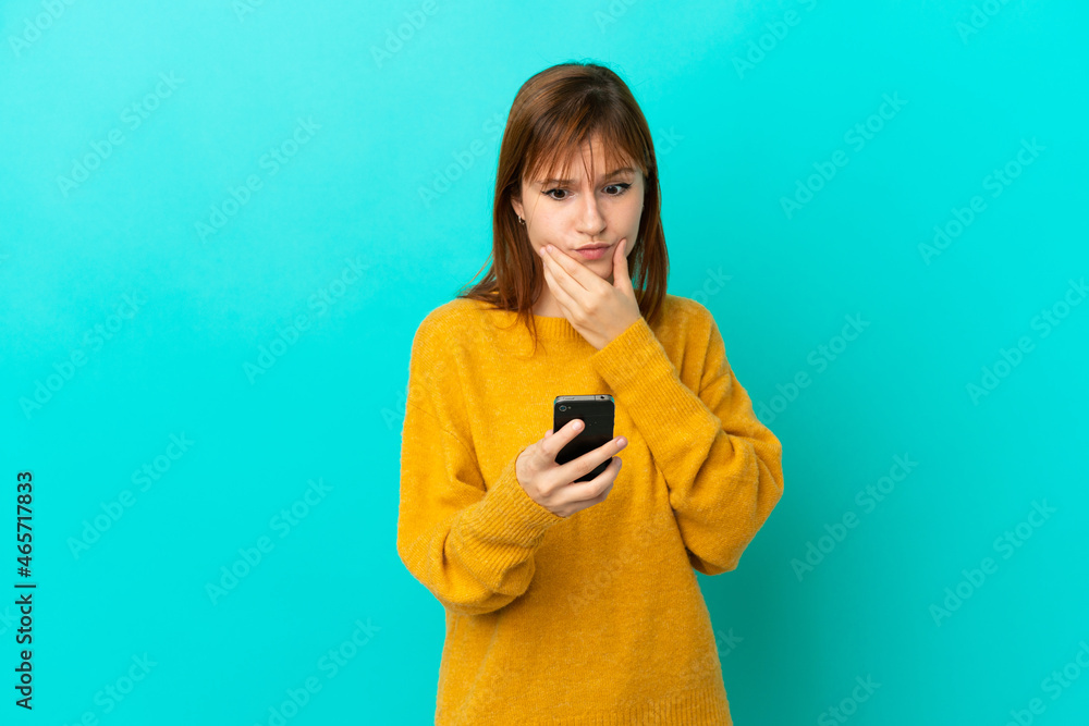 Redhead girl isolated on blue background thinking and sending a message Redhead girl isolated on blue background thinking and sending a message