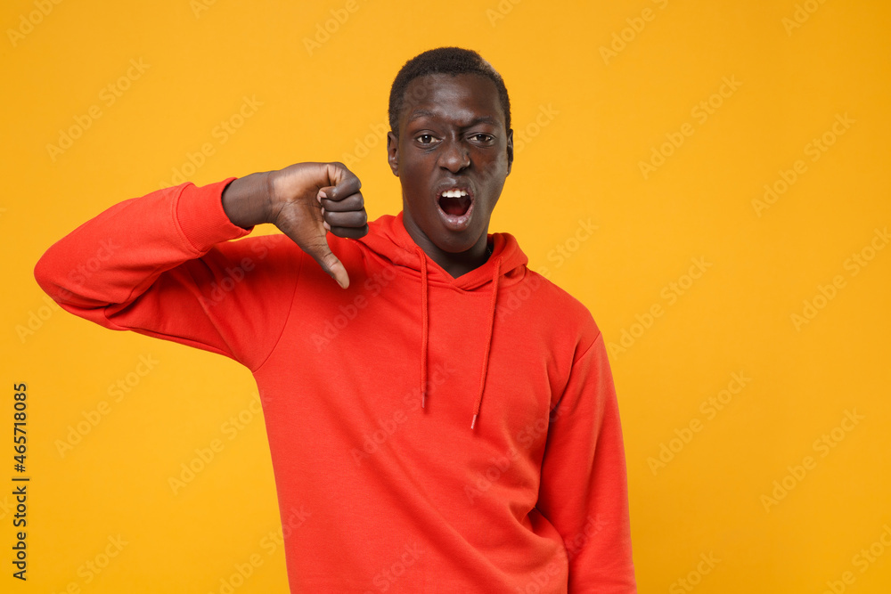 Dissatisfied young african american man guy in red streetwear hoodie posing isolated on yellow background studio portrait. People emotions lifestyle concept. Mock up copy space. Showing thumb down. Dissatisfied young african american man guy in red streetwear hoodie posing isolated on yellow background studio portrait. People emotions lifestyle concept. Mock up copy space. Showing thumb down.