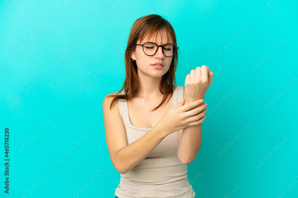 Redhead girl isolated on blue background suffering from pain in hands Redhead girl isolated on blue background suffering from pain in hands