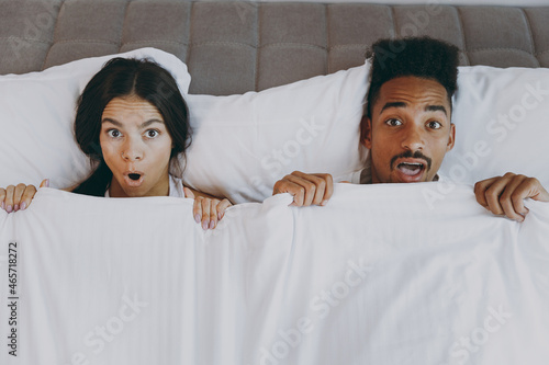 Top view surprised young couple two friends family man woman in casual white clothes lying in bedhold blanket look camera rest relax spend time together in bedroom home room house wake up good day. photo