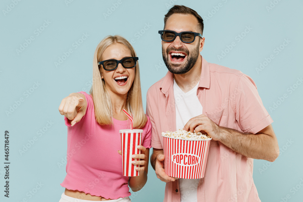 Obraz premium Young couple family man woman friends in 3d glasses watch movie film hold bucket of popcorn cup of soda pop laugh isolated on plain blue background studio People emotion in cinema lifestyle concept