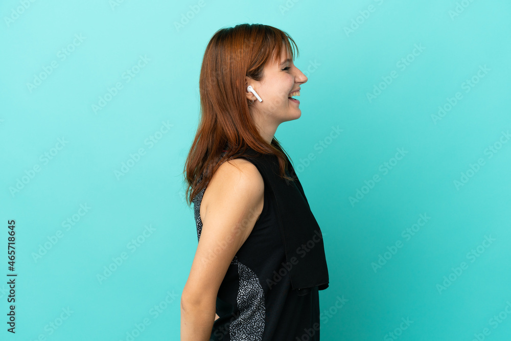 Redhead sport girl isolated on blue background laughing in lateral position Redhead sport girl isolated on blue background laughing in lateral position