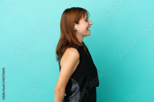 Redhead sport girl isolated on blue background laughing in lateral position