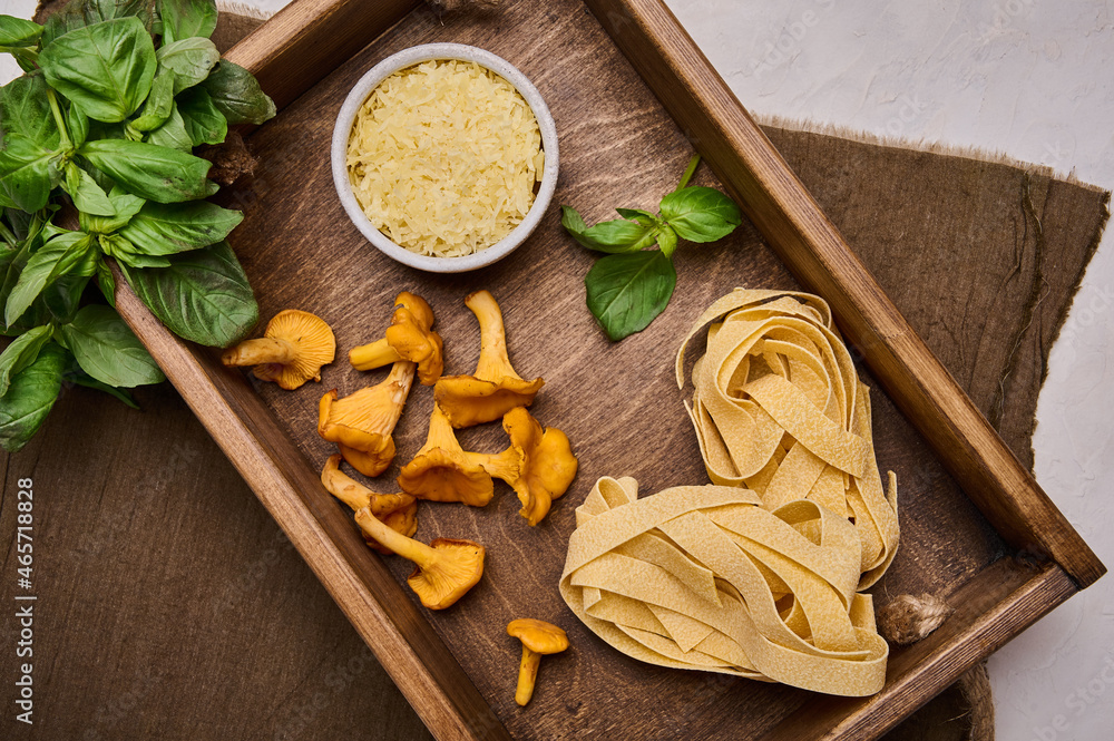 Fototapeta premium Raw ingredients for making Italian pasta pappardelle with mushrooms chanterelles and cheese in rustic wooden tray on linen napkin, top view flat lay