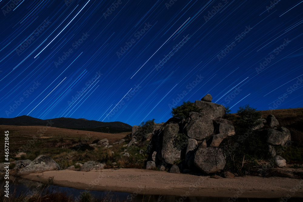 Obraz premium Star trail over creek and rocky outcrop with moonlight illuminating landscape