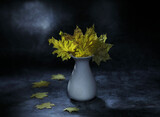 Still life with yellow maple leaves in a white ceramic vase on a dark background.